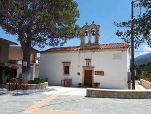 A white building with a bell tower, a stone bench, and a paved courtyard. - Koukos House surrounded be nature (Chania)
