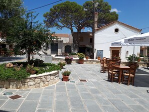 An outdoor seating area with stone flooring, potted plants, and wooden furniture. - Koukos House surrounded be nature (Chania)