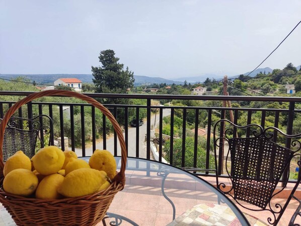 A balcony with a wicker basket of lemons, a metal chair, and a view of a hilly landscape. - Koukos House surrounded be nature (Chania)