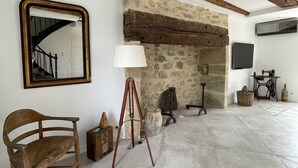 A spacious room with a stone wall, wooden beams, a large mirror, a tripod, a lamp, a vintage sewing machine, and a wicker basket.