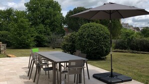 An outdoor patio with a table and chairs, a large umbrella, and a stone-tiled floor.