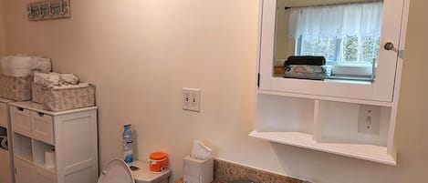 A bathroom with a sink, mirror, and toilet. There are storage cabinets and a window with a view.