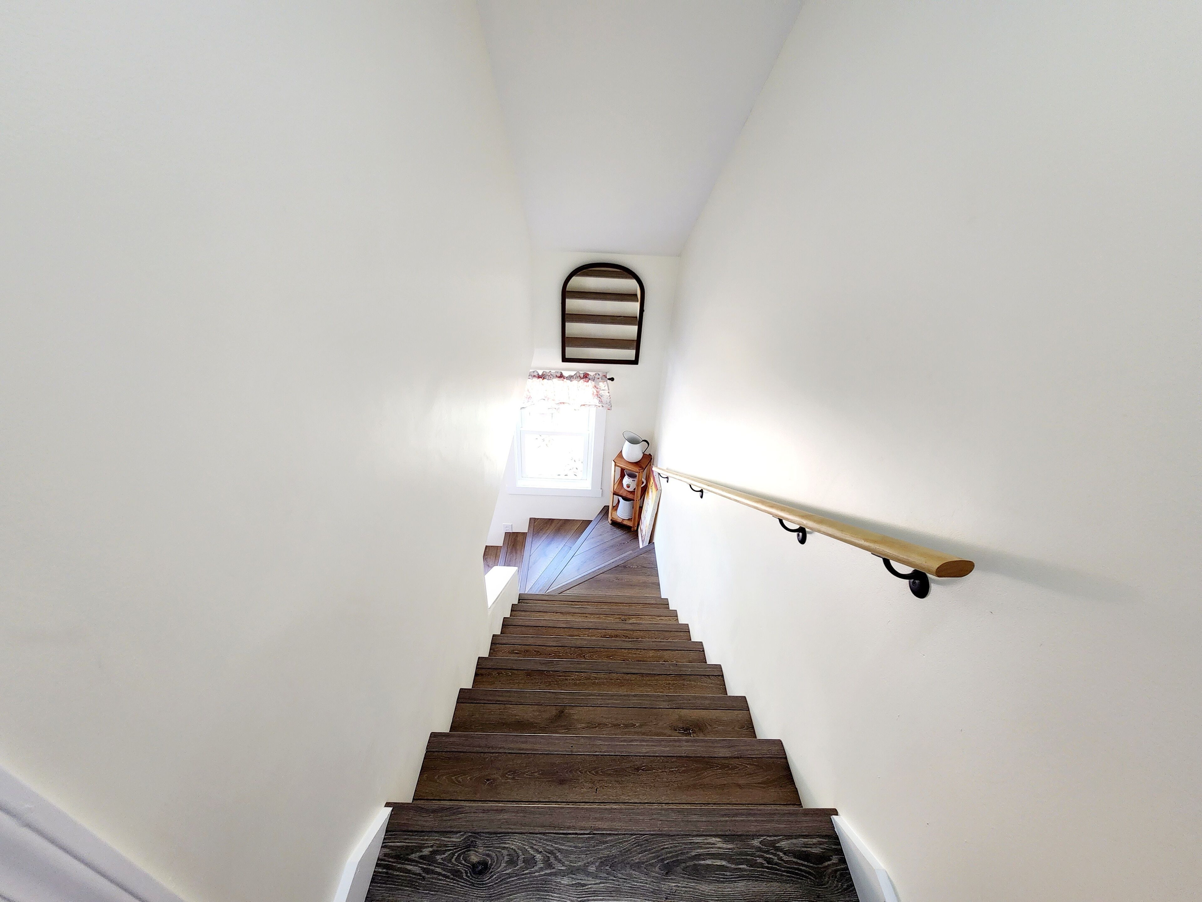 A wooden staircase with a handrail, white walls, and a window at the top.