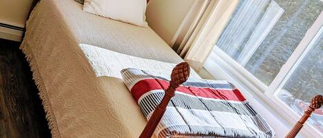 Una cama bien hecha con cabecera de madera, una ventana con cortinas y un cuadro enmarcado en la pared.