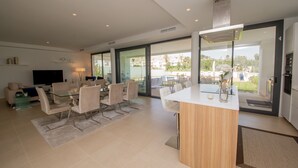 A modern living room with a glass dining area, a sofa, and a flat-screen TV.