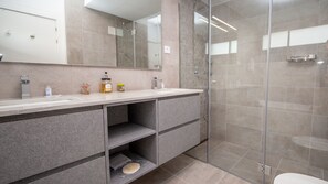Een moderne badkamer met een douchecabine van glas, een grote spiegel en een wastafelmeubel met een wastafel en opbergladen.
