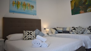 A hotel room with two beds, a headboard, a nightstand, a lamp, and artwork on the walls.