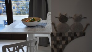 A dining area with a white table, a bowl of fruit, and a wall decoration of two cat figures.