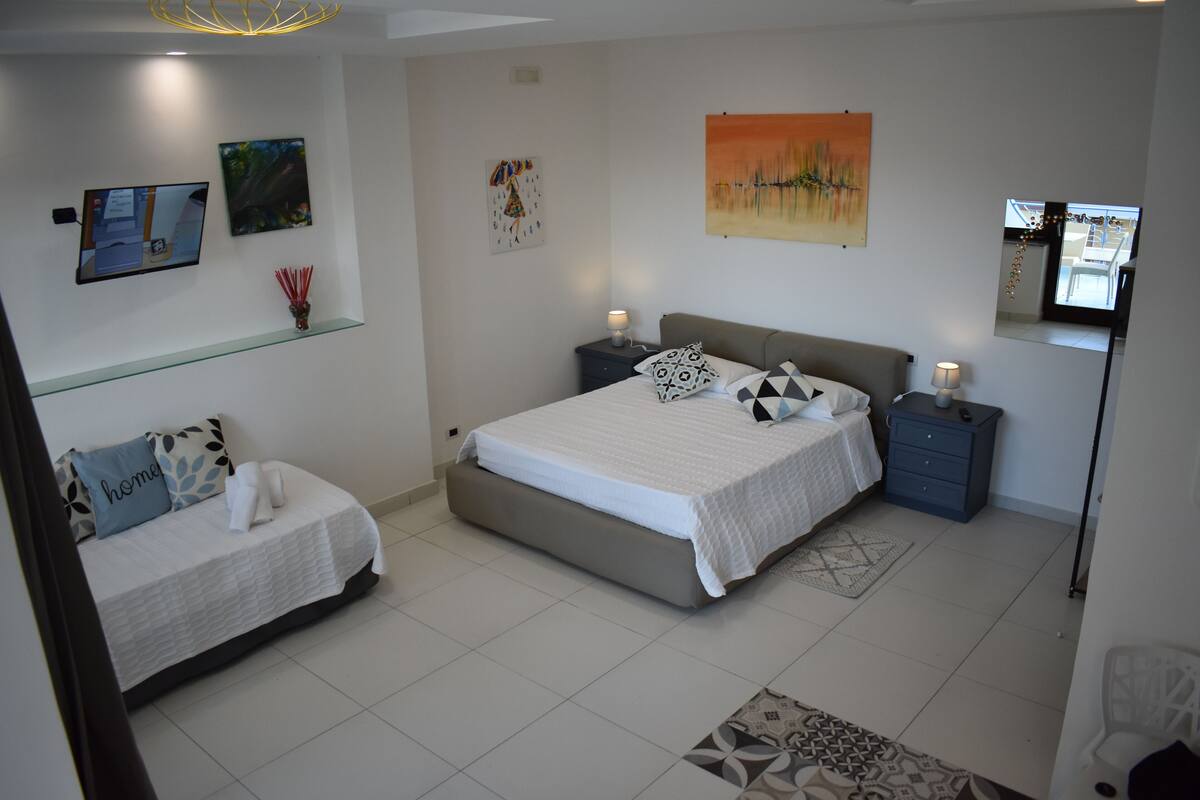 A bedroom with a bed, two bedside tables, a TV, and artwork on the walls.