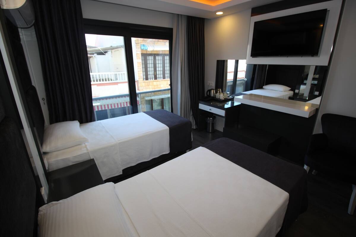 Habitación de hotel con dos camas, un escritorio, televisor y vistas al balcón.