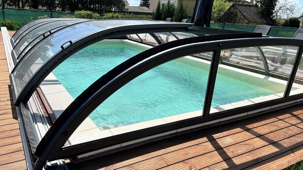 Une piscine dotée d’une enceinte en verre et d’une terrasse en bois.