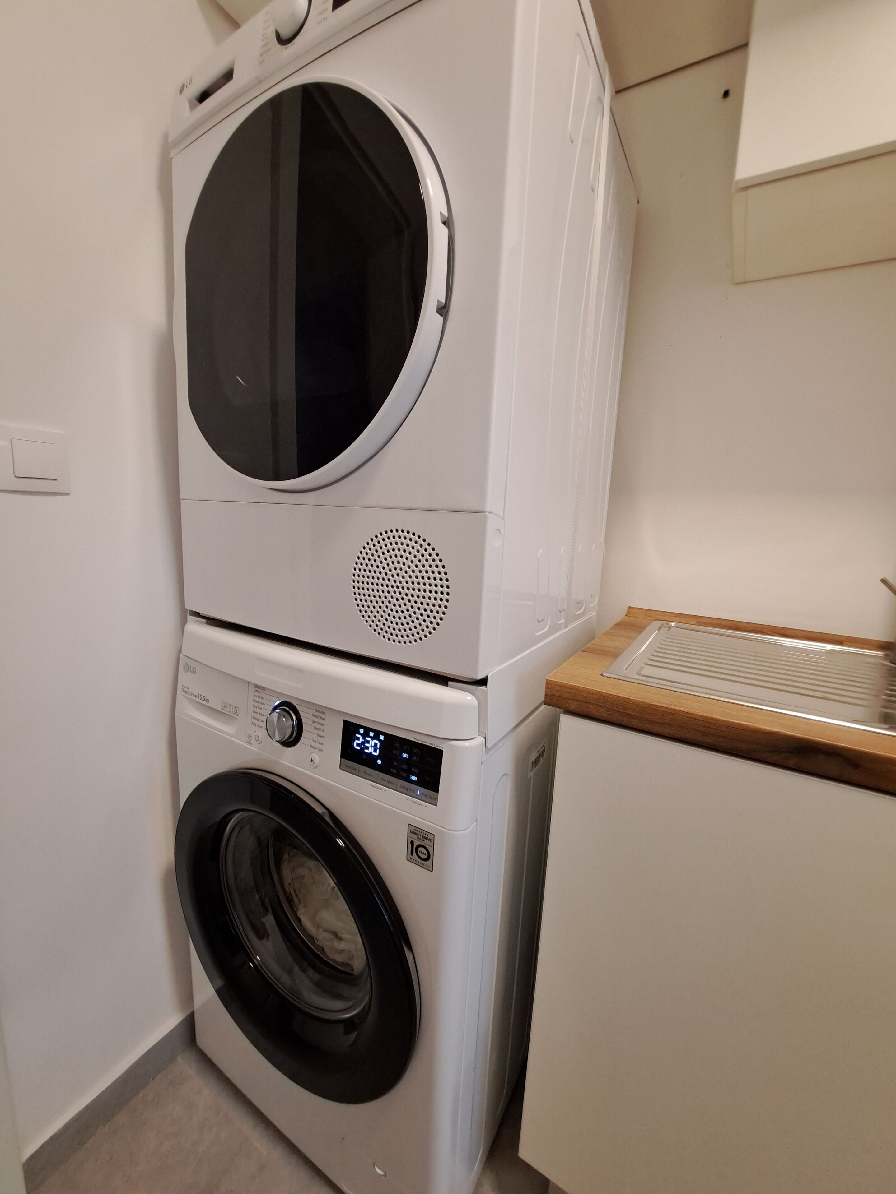 Un appareil combiné lave-linge et sèche-linge, de type « empilable », doté d’un écran numérique, d’un panneau de commande et d’un plan de travail en bois.