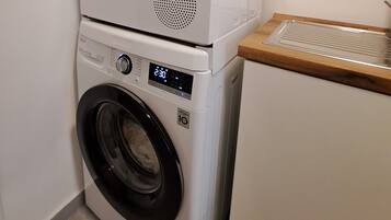 Un appareil combiné lave-linge et sèche-linge, de type « empilable », doté d’un écran numérique, d’un panneau de commande et d’un plan de travail en bois.