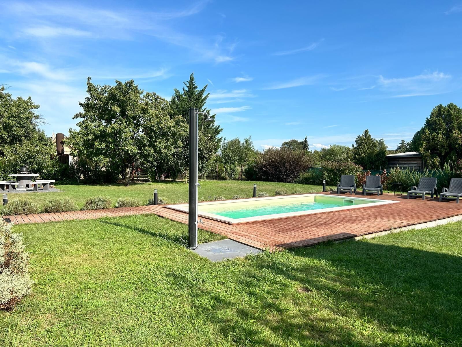 A rectangular swimming pool with a wooden deck surrounding it, a picnic table, and outdoor seating.