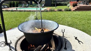 Un ensemble de cuisine d’extérieur portatif, avec une marmite placée sur un feu, entouré d’une pelouse et avec une piscine en arrière-plan.