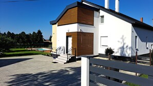 Une maison moderne avec une façade blanche, une partie recouverte de lambris en bois et un escalier apparent menant à l’entrée.