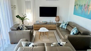Un salon moderne avec un téléviseur à écran plat, des canapés en cuir, une table basse et un tableau accroché au mur.
