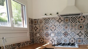 A kitchen with patterned tiles, a sink, a stove, and storage cabinets. - LA CABANE AUX ECREVISSES- FEET IN THE WATER (Châteauneuf-les-Bains)