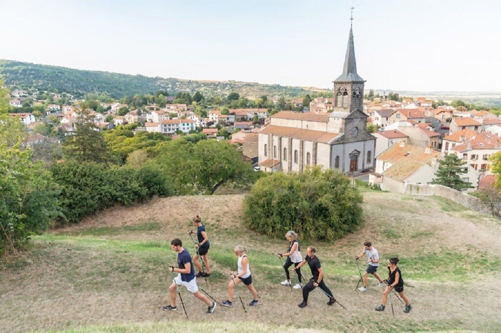 Eine Gruppe Wanderer auf einem grasbewachsen Hügel, im Hintergrund eine Kirche und Wohnhäuser.