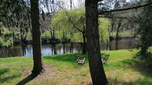 A serene lakeside setting with two wooden chairs facing the water, surrounded by lush greenery and trees. - LA CABANE AUX ECREVISSES- FEET IN THE WATER (Châteauneuf-les-Bains)