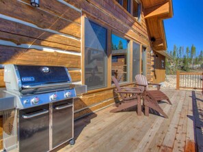 Una terraza de madera con una parrilla y sillas Adirondack.