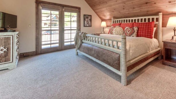 A bedroom with a wooden ceiling, a bed with red and white bedding, a nightstand, and a dresser. - Luxury 5 Bedroom Big Sky Retreat (Big Sky)