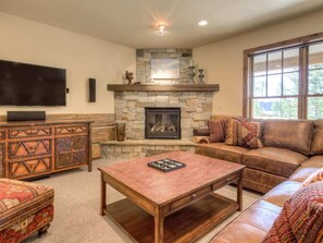 A cozy living room with a stone fireplace, leather sofa, and a flat-screen TV. - Luxury 5 Bedroom Big Sky Retreat (Big Sky)