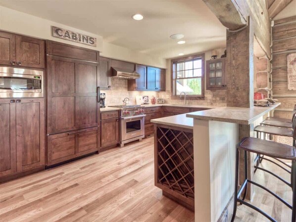 Una cocina con armarios de madera, horno de acero inoxidable, una bodega y una zona de bar con taburetes.
