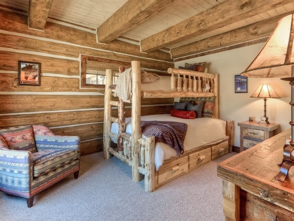 A rustic cabin interior with a bunk bed, a wooden desk, a chair, and a lamp.
