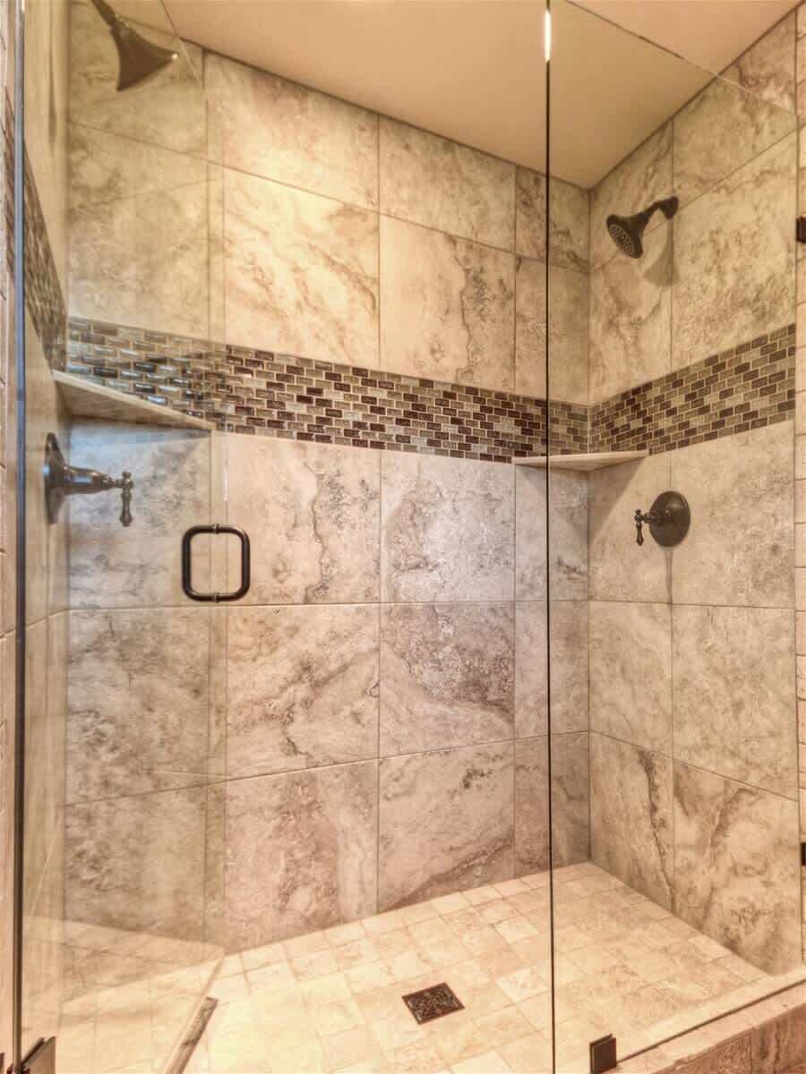 Une douche entièrementClose avec des parois en verre, des carreaux de marbre et une bordure décorative en briques.