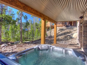 Un jacuzzi en una cabaña de madera con vistas a un bosque y una montaña al fondo.