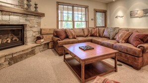 A cozy living room with a stone fireplace, a large L-shaped sectional sofa, and a wooden coffee table. - Luxury 5 Bedroom Big Sky Retreat (Big Sky)