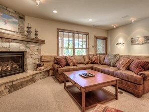 A cozy living room with a stone fireplace, a large L-shaped sectional sofa, and a wooden coffee table.