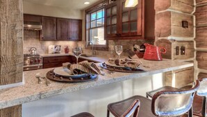 A rustic kitchen with wooden cabinets, a stone wall, and a bar area with stools. - Luxury 5 Bedroom Big Sky Retreat (Big Sky)