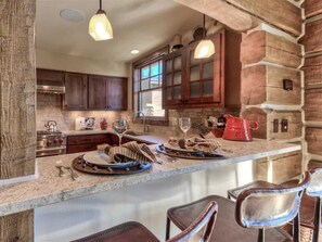 A rustic kitchen with wooden cabinets, a stone wall, and a bar area with stools.