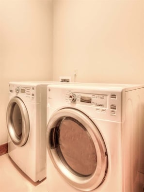 Two front-loading washing machines in a laundry room with a plain wall and a power outlet.