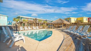 A pool area with lounge chairs and a thatched roof structure. - Mermaid Cove PA! Beach Gear Credit, Community Pool (Port Aransas)