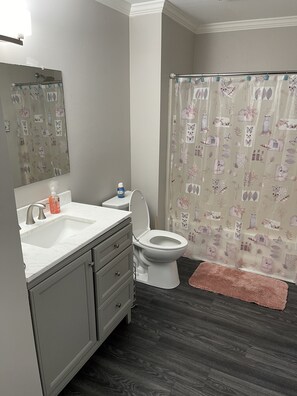 A bathroom with a white toilet, a sink with a mirror above it, and a shower curtain with a floral pattern. - Luxury 3bd/2ba Beach Condo on Golf Course (Myrtle Beach)