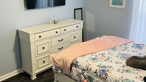 A bedroom with a bed, dresser, ceiling fan, TV, and wall art. - Luxury 3bd/2ba Beach Condo on Golf Course (Myrtle Beach)