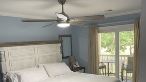 A bedroom with a bed, a ceiling fan, a nightstand, a mirror, and a view of the outdoors. - Luxury 3bd/2ba Beach Condo on Golf Course (Myrtle Beach)
