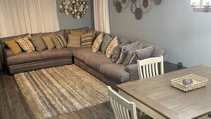 A modern living room with a sectional sofa, a dining table with chairs, a patterned rug, and decorative wall art. - Luxury 3bd/2ba Beach Condo on Golf Course (Myrtle Beach)