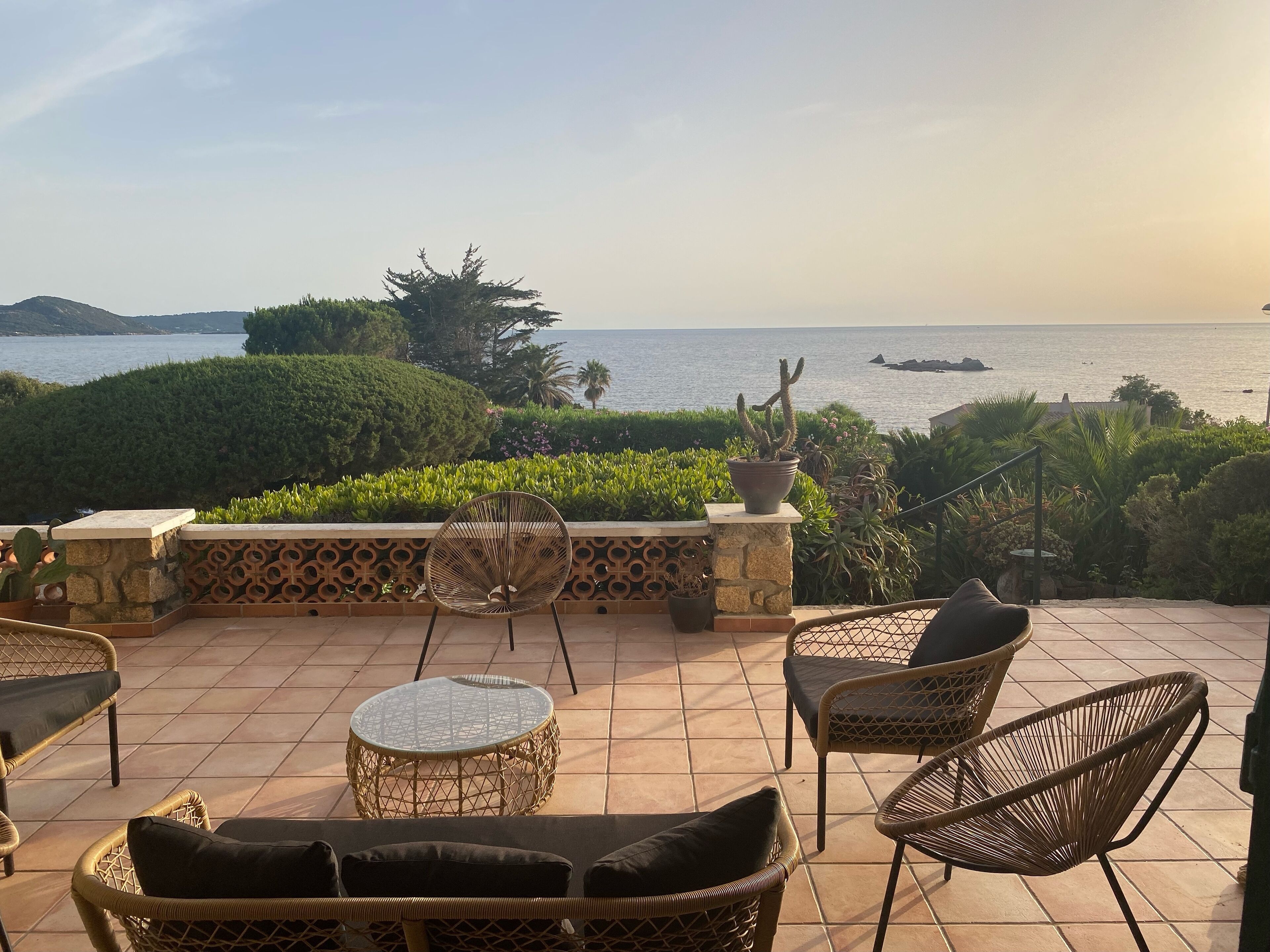 A terrace with wicker furniture, a round glass table, and a view of the sea.