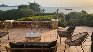 Terraço com mobiliário de vime, uma mesa redonda de vidro e vista para o mar.