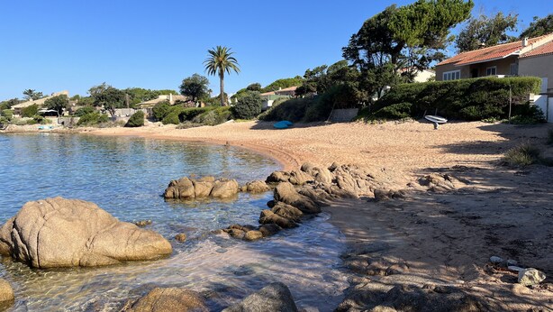 Uma praia com águas cristalinas, rochas grandes e areal arenoso.