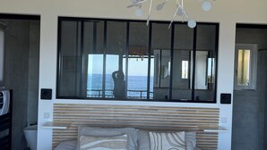 Quarto moderno com uma cama grande, uma luminária de teto original, vista para o mar por uma janela ampla e um design minimalista.