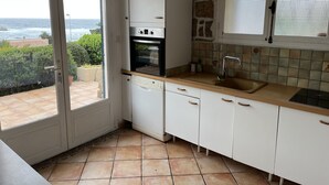 Cozinha com armários brancos, forno embutido, pia e janela com vista panorâmica.