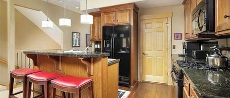 Una cocina con armarios de madera, un refrigerador negro, una estufa y una barra con taburetes rojos.