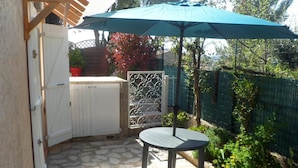 A patio with a table and umbrella, stone flooring, a white gate, and a green fence. - House with pool in Le Pradet quiet location  (Le Pradet)