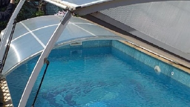 A swimming pool with a retractable roof, surrounded by a stone wall and a building with a tiled roof. - House with pool in Le Pradet quiet location  (Le Pradet)