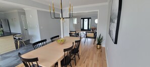 Un espace repas avec une longue table, des chaises noires, un lustre et une plante en pot.